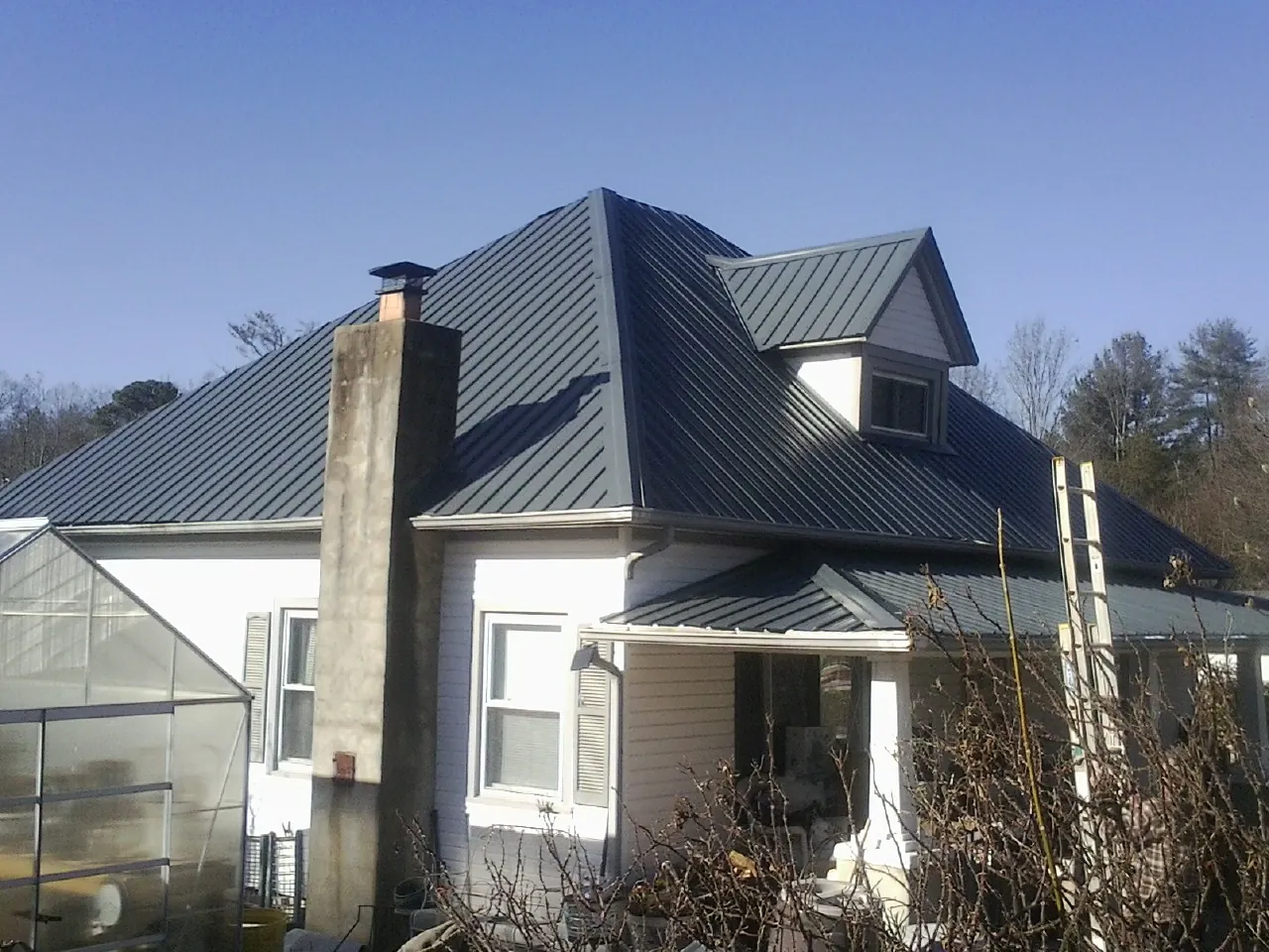 Dark blue standing seam metal roof on a white farmhouse with dormer — Slate & Tile Roof Repair by Roofing Brothers in Sylacauga