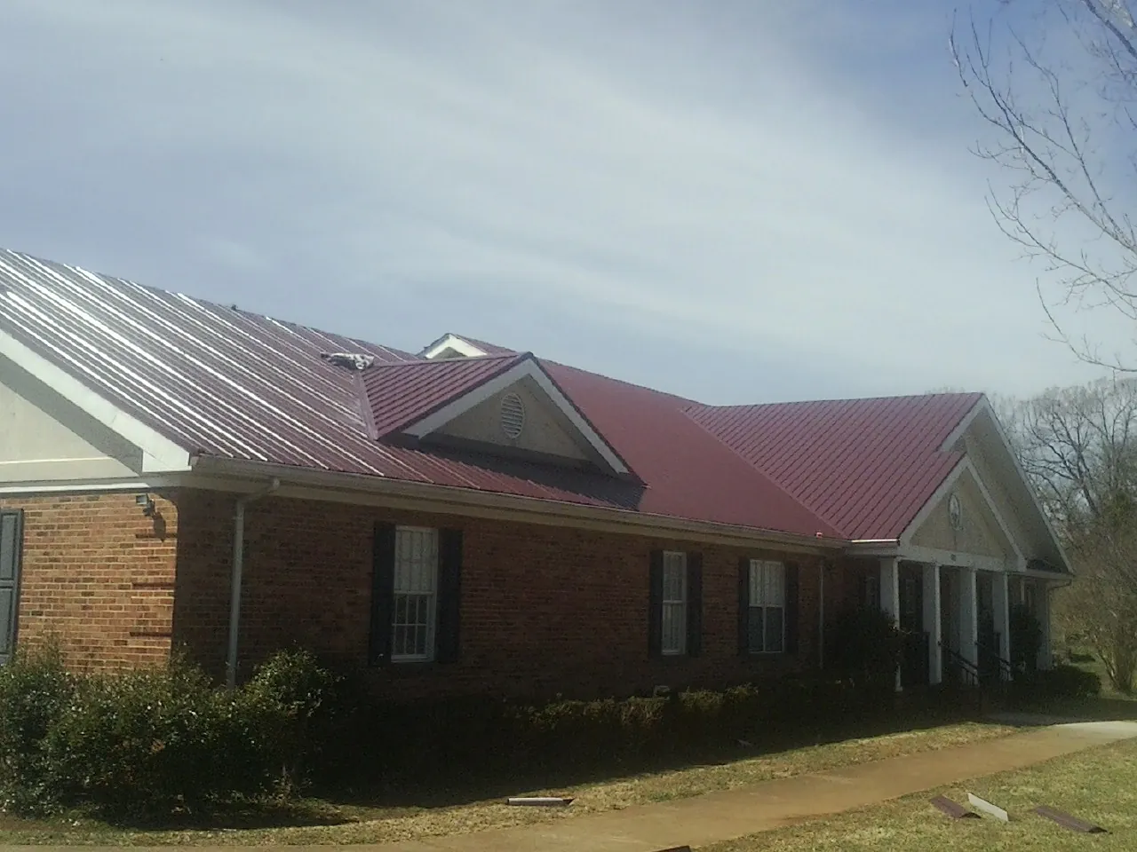 Red metal roof with gabled entries on a long brick building, from a Hail Damage Roof Repair job in Sylacauga