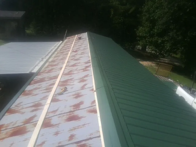 Old rusted panels beside newly installed green metal roofing — Wind Damage Roof Repair by Roofing Brothers in Sylacauga