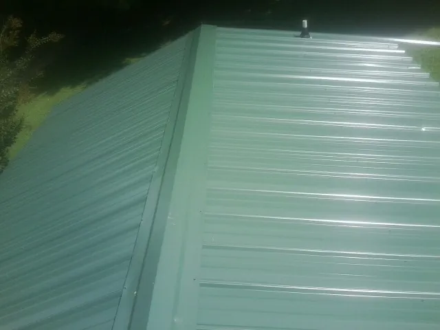 New green metal panels meeting at the ridge of a roof — Flat Roof Repair work by our crew in Sylacauga