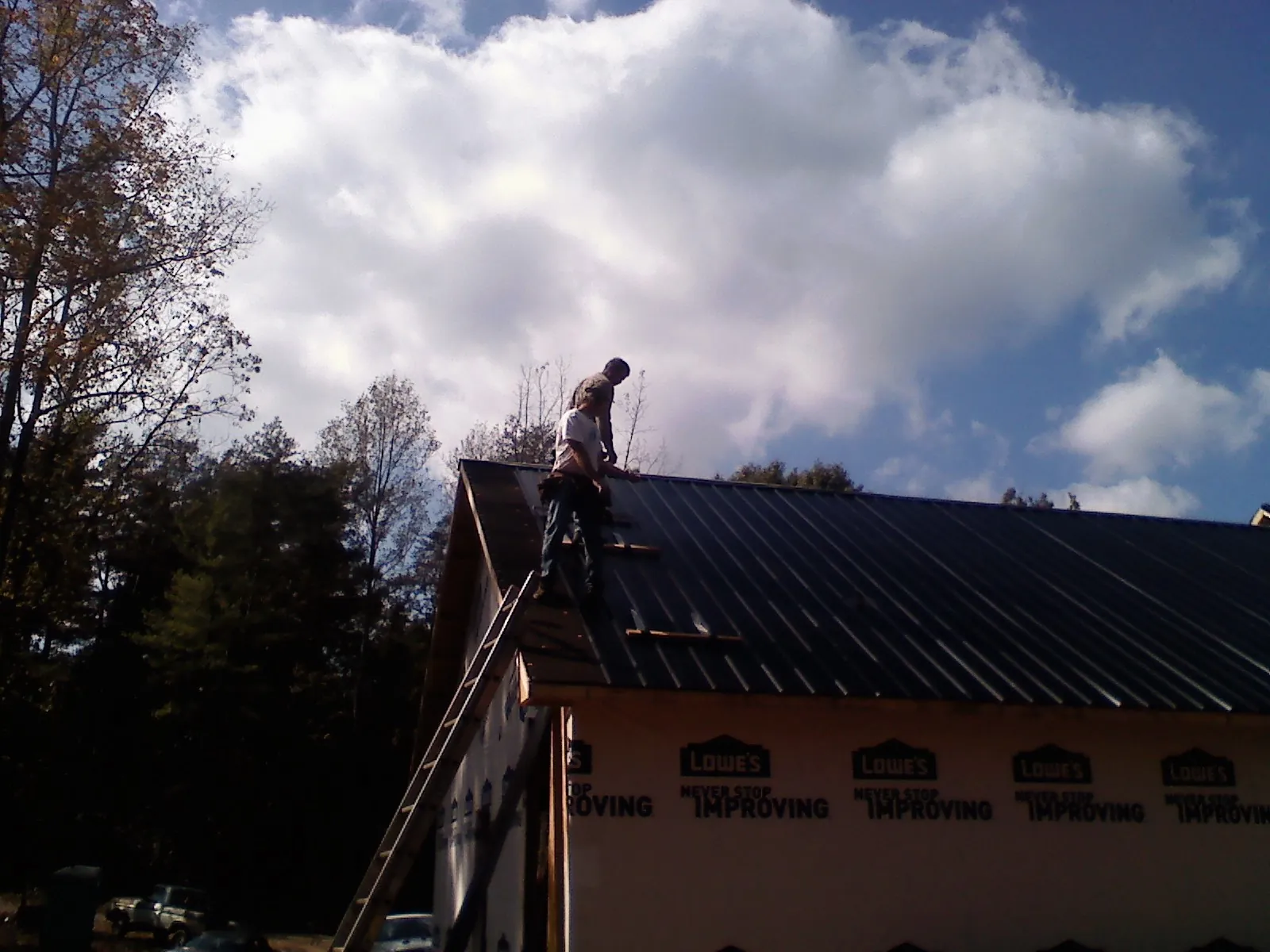 Roofer fastening dark metal panels high against a cloudy sky, from a Roof Inspection job in Sylacauga