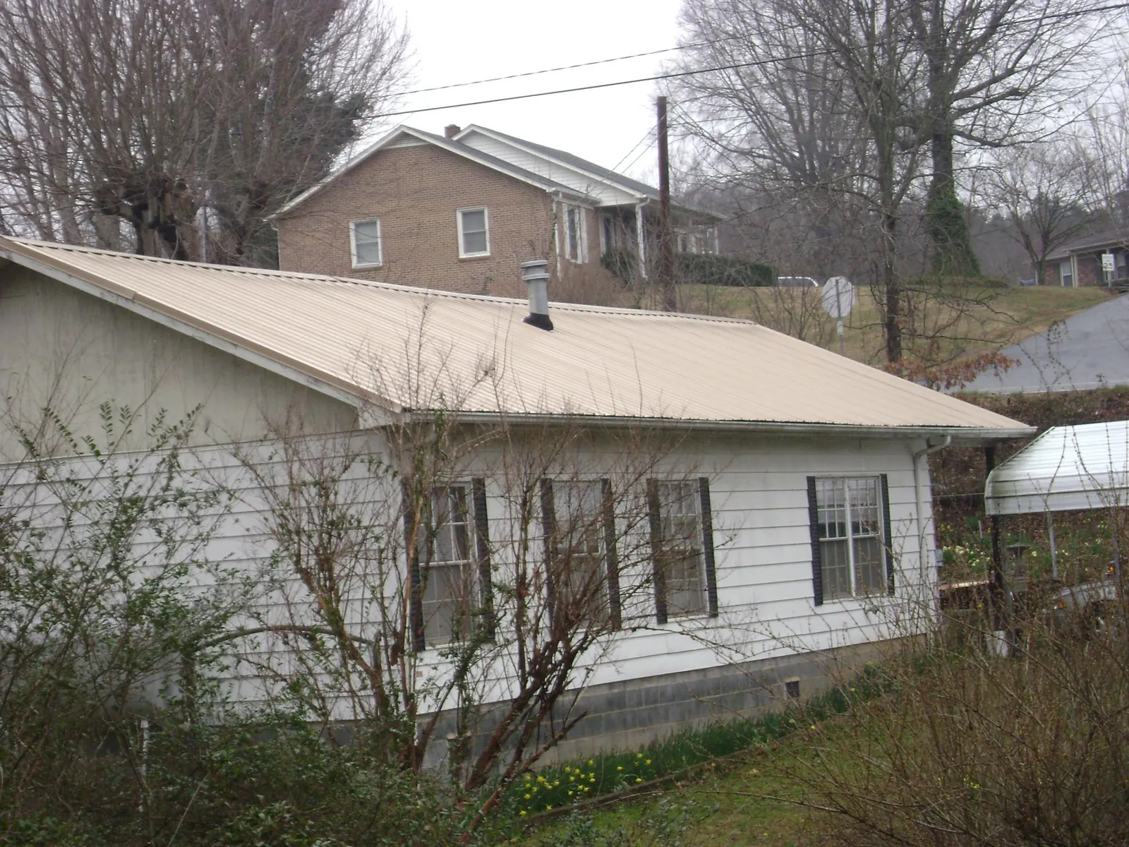 Tan metal roof on a white sided house set into a hillside — Commercial Roofing by Roofing Brothers in Sylacauga