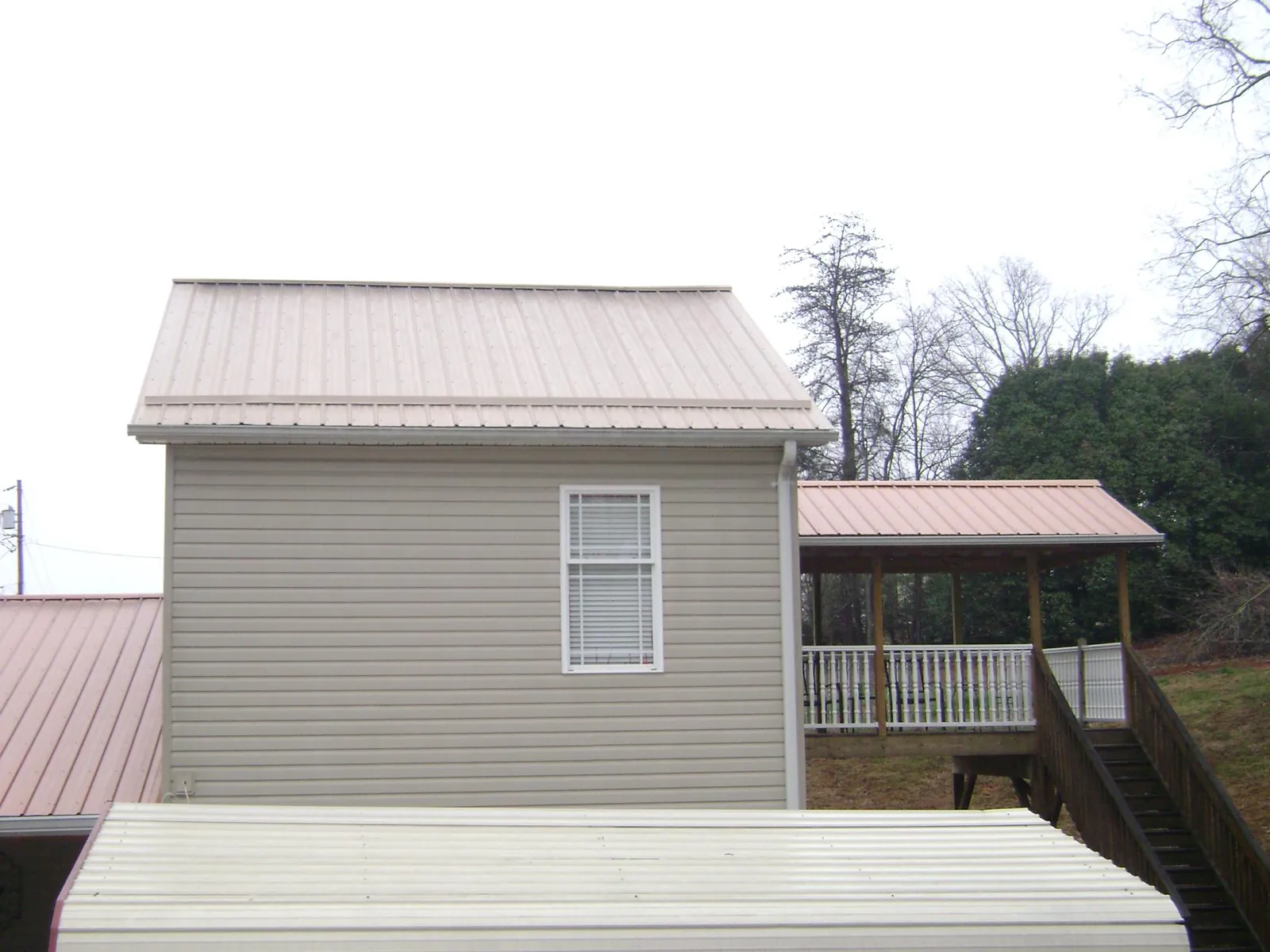Tan metal roofs on a two story addition and attached porch, from a Roof Replacement job in Sylacauga
