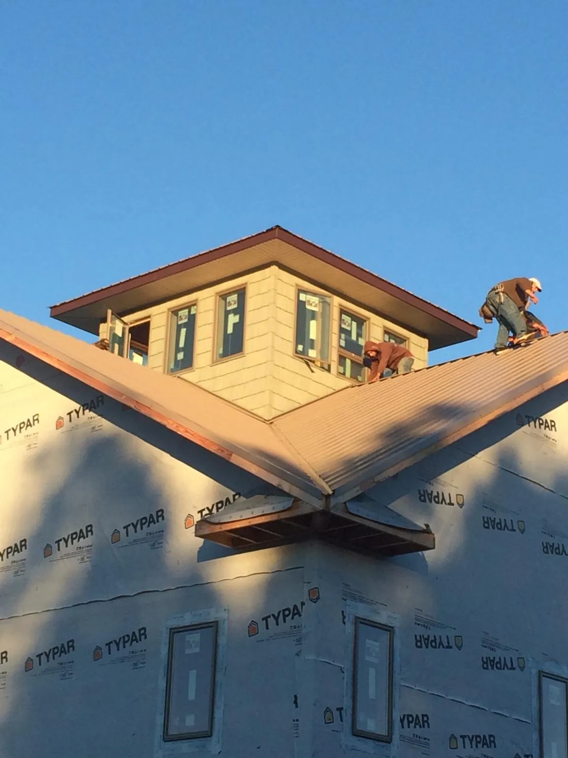 Roofers working around a rooftop cupola on a new metal roof at sunset — Roof Waterproofing in Sylacauga by Roofing Brothers